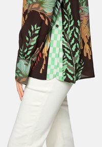 Short-sleeved shirt with a brown background featuring green and red leaf patterns and a contrasting green checkered underlayer.