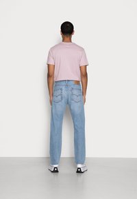 T-shirt de manga curta rosa claro, jeans de ganga azuis e sapatilhas pretas e brancas. Os jeans têm bolsos traseiros distintos e um patch de pele.