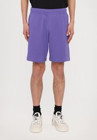 Pantalones cortos de algodón morado con cintura elástica, corte ajustado y bolsillos laterales. Presenta una marca en la pierna derecha.