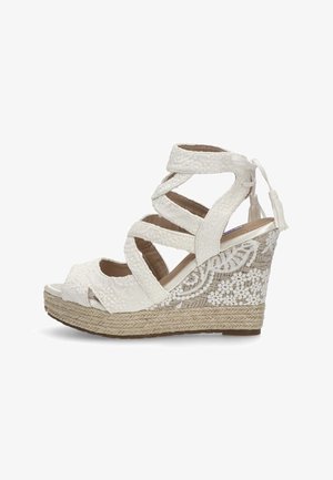 Sandalia de cuña blanca con un tacón de yute trenzado, intrincados acentos de encaje floral y correas cruzadas ajustables. Diseño de punta abierta.