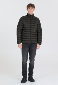 Svart vadderad jacka med hög krage, med horisontella quiltade sektioner, framsidan med dragkedja, bärs över mörka jeans och svarta skor.