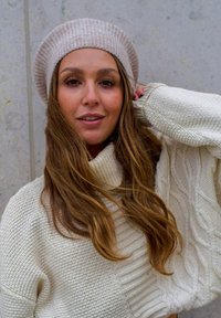Cable-knit cream sweater with loose fit and ribbed cuffs, paired with a light beige ribbed beret. Smooth texture and subtle color contrast.