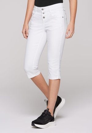 White cropped jeans with button fly, front pockets, and hemmed cuffs. Paired with black athletic sneakers, featuring a mesh upper and white sole.