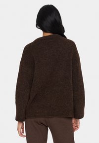 Mörkbrun stickad tröja med avslappnad passform, sänkta axlar och en strukturerad yta; inga synliga detaljer eller mönster.