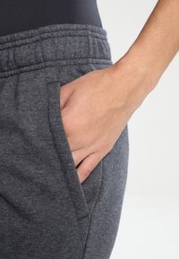 Grijze sweatpants met een elastische tailleband en een zijzak, gemaakt van een zachte, gestructureerde stof. Hand ligt comfortabel in de zak.