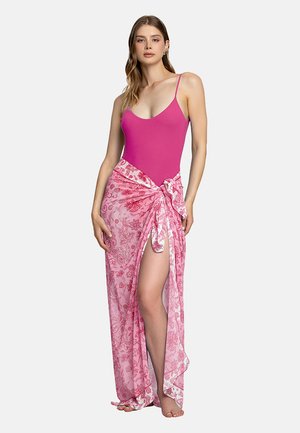 Costume intero rosa con spalline sottili, abbinato a un sarong rosa chiaro a fantasia legato in vita, che presenta disegni floreali e uno spacco laterale.