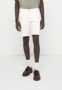 Fehér farmer rövidnadrág egyenes fazonnal, közepes derékvonallal és öt zsebbel, barna bőr cipővel és fehér bokaszakállal párosítva.