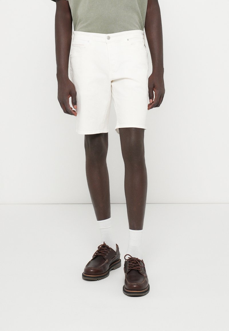 Fehér farmer rövidnadrág egyenes fazonnal, közepes derékvonallal és öt zsebbel, barna bőr cipővel és fehér bokaszakállal párosítva.