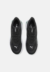 Baskets de sport noires avec tige en mesh, design à lacets et semelle en caoutchouc blanc. Présentent un accent vert au niveau du talon et un logo sur la languette.