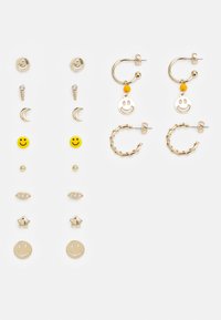 Brincos em tom dourado com studs de rosto sorridente, pendentes em forma de lua crescente, acentos sorridentes amarelos e designs de argolas texturizadas.