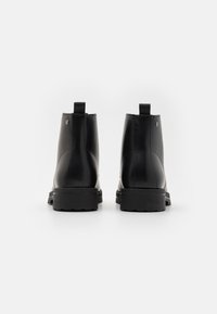 Botas de cuero negro hasta el tobillo con un acabado suave, punta redonda, tirador trasero y suelas de goma texturizadas. Cuenta con detalles de costura sutiles.