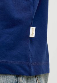 Camiseta de algodón azul marino con mangas cortas, que presenta una etiqueta lateral marcada como "Originals" y un detalle de dobladillo cosido.