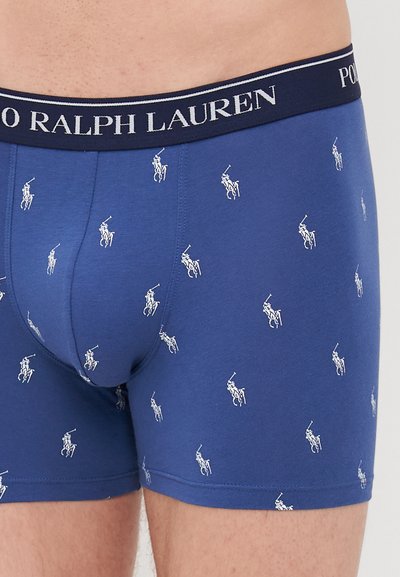 Sötétkék boxernadrág, puha anyagból készült, ismétlődő fehér póló játékos mintával, rugalmas derékkal, amelyen a 'Polo Ralph Lauren' márkaneve szerepel.
