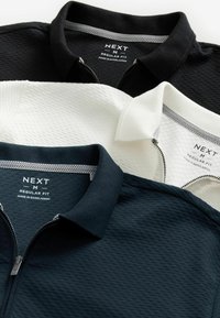 Drie poloshirts in zwart, wit en marineblauw. Elk shirt heeft een textuurdesign, een ritskraag en 'NEXT' branding op het binnenlabel.