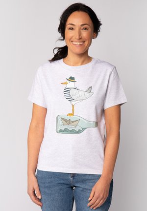 T-shirt en coton gris clair avec un dessin de mouette en cartoon portant une chemise rayée et un chapeau, se tenant sur une bouteille avec un bateau en papier à l'intérieur.