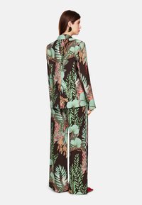 Blumendesign-Anzug in Schwarz mit Grüntönen, Rot und Koralle. Lockere Passform mit langen Ärmeln und weitem Hosenschnitt. Glatte Stoffqualität.