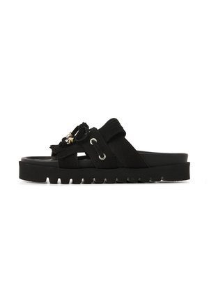 Black slide sandal with thick ridged sole, two wide straps including one with metal eyelets and decorative tassels with beads.