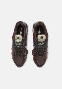 Paire de baskets Nike Shox marron foncé avec des lacets bleus et des étiquettes de languette beige, vues de dessus sur un fond blanc.