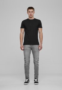 Musta puuvillainen t-paita yhdistettynä rikkinäisiin harmaisiin farkkuihin. Mallilla on päällään mustat ja valkoiset urheilukengät. Slim fit -mallinen, jossa pyöreä kaula-aukko.