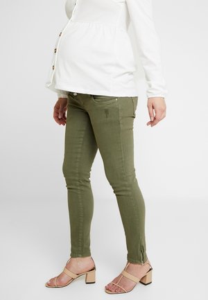 Těhotná osoba oblečená v bílém zapínaném topu, olivově zelených úzkých kalhotách s zipy na kotnících a béžových sandálech s blokovým podpatkem a otevřenou špičkou.