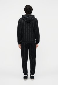 Conjunto de sudadera con capucha y pantalones deportivos negros con estampado repetido de logo. Tejido suave con un ajuste relajado y capucha ajustable.