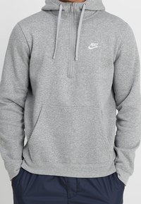 Grå zip-up hoodie i mjuk fleece. Har en framficka i kängurustil, dragsko i huvan och en liten vit Nike-logotyp på bröstet.