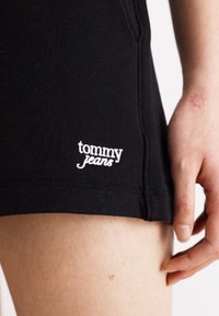 Sorte bomullsshorts med tett passform, med en hvit "tommy jeans" logo sydd på siden. Glatt tekstur og minimalistisk design.