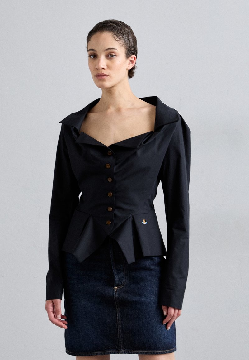 Μαύρη βαμβακερή μπλούζα με μεγάλο γιακά, κουμπιά μπροστά και λεπτομέρειες πτυχών στο στρίφωμα. Συνδυασμένη με φούστα από σκούρο τζιν, με επιμελημένο σχέδιο.