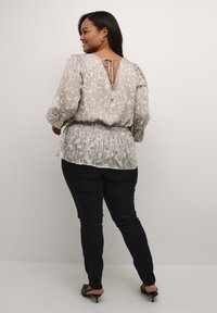 Blusa grigia chiaro con motivo astratto, vita arricciata e design con retro a V con chiusura a fiocco, abbinata a jeans skinny neri e tacchi.