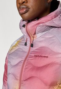 Ελαφρύ μπουφάν puffer με ροζ και κίτρινο διαβαθμισμένο χρώμα, κλείσιμο με φερμουάρ, καπιτονέ σχέδιο και ρυθμιζόμενο κουκούλι. Διαθέτει το λογότυπο "Peak Performance".