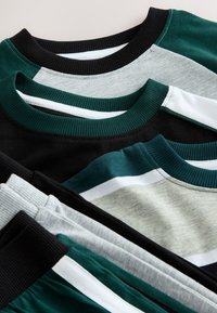 Pile de chemises décontractées pliées avec cols ronds en blocs de couleurs noir, vert, gris et blanc et motifs rayés.