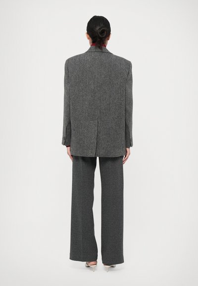 Grå textil kostym med skräddarsydd kavaj och vida byxor. Utmärkande för sin texturerade tyg och strukturerade silhuett. Silverklackar synliga.
