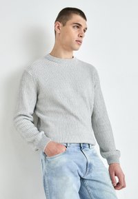 Grå ribbestrikket genser med rund hals, lange ermer og avslappet passform, kombinert med lyseblå denimjeans.