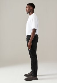 T-shirt bianco a maniche corte abbinato a pantaloni slim-fit neri e scarpe stringate marroni. Il tessuto appare liscio con una vestibilità strutturata.