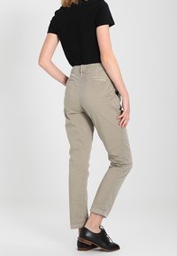 Chinos color beige chiaro con vestibilità slim, caratterizzati da vita, tasche posteriori e una texture liscia, abbinati a scarpe nere con lacci.