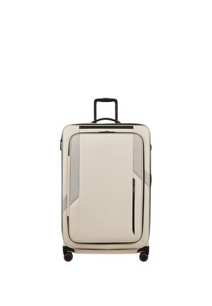 Großer beiger Koffer mit schwarzem Teleskopgriff, Frontreißverschlusstasche und vier schwarzen Rädern mit roten Akzenten, aufrecht stehend.