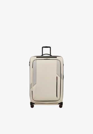 Large beige suitcase with black telescopic handle, front zippered pocket, and four black wheels with red accents, standing upright.