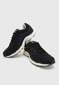 Zapatillas deportivas negras con una parte superior de malla texturizada, suela acolchada y acentos en blanco contrastante. Cintas y logotipo en la lengüeta.