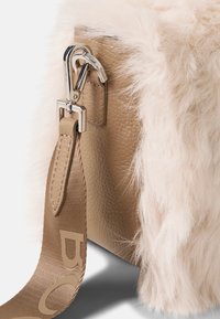 Lædertaske med bløde hvide pelsdetaljer, udstyret med en sølvklemme og en beige strop med præget logo. Tekstureret overflade og moderne design.