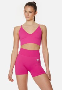 Ružová športová podprsenka s tenkými ramienkami a V-krkom, v kombinácii s vhodnými šortkami s vysokým pásom a bielym logom.