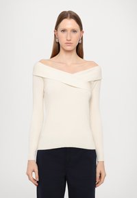 Top justo off-white com ombros à mostra, mangas longas, textura canelada e design de gola dobrada. Combinado com calças escuras. Simples e elegante.