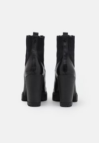 Bottes cheville noires avec une finition en cuir et un tissu tricoté en haut, talons blocs, et boutons fonctionnels à l'arrière.