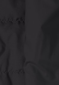 Close-up of black quilted jacket fabric showing stitched seams and textured material with a subtle grid pattern.