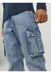 Blue denim cargo pants with a relaxed fit, featuring large side pockets and visible stitching details. Material has a soft, worn texture.