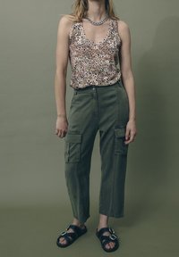 Top de tirantes con lentejuelas en rosa claro con manchas de leopardo, combinado con pantalones cargo verde oliva con bolsillos laterales y sandalias negras con hebilla.