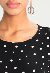 Black top with white polka dots, featuring a round neckline and smooth texture, paired with a large circular earring.
