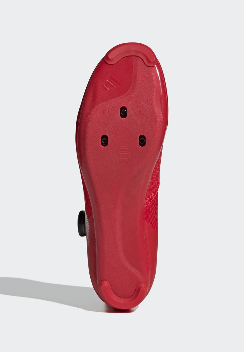 Rote Fahrradschuhsohle mit strukturiertem Gummi und fünf Cleat-Löchern, einer glatten Oberseite und einem erhöhten Absatz für Stabilität.
