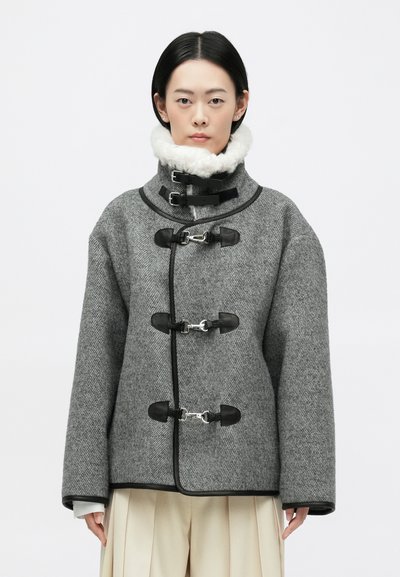 Manteau en laine grise avec un motif en herringbone texturé, accents en cuir noir, grand col et fermetures à bascule. Silhouette en A avec des manches larges.