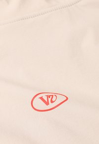 Tessuto color crema con una texture liscia presenta un logo ovale rosso con le lettere "V" e "U" in evidenza.