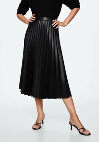 Jupe plissée en faux cuir noir avec une taille haute, longueur genoux, dotée d'une texture lisse et d'une finition brillante.
